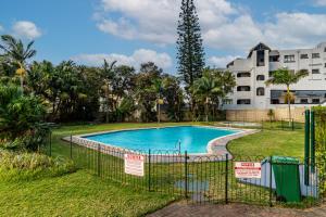 a fence around a swimming pool in front of a building at Cosy Sky View Apartment in Ballito