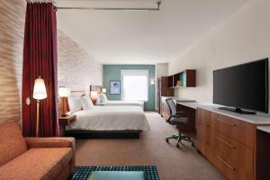 a hotel room with a bed and a desk with a television at Home2 Suites By Hilton Lancaster in Lancaster
