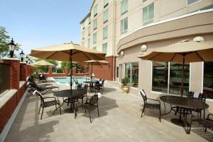 un patio al aire libre con mesas, sillas y sombrillas en Hilton Garden Inn Harrisburg East en Harrisburg