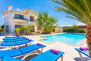 a villa with a swimming pool and blue lounge chairs at Villa Dora in Argaka