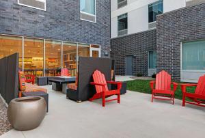 Home2 Suites By Hilton Milwaukee Downtown في ميلووكي: فناء به كراسي حمراء وطاولات أمام مبنى