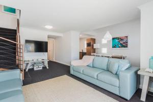 a living room with a blue couch and a tv at Midd's on the Beach - luxury beach front apartment in Albany