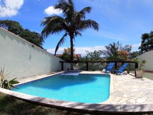 a swimming pool with two chairs and a palm tree at Pousada Tehau Guest House in Búzios