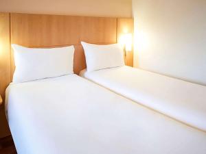 2 camas en una habitación con sábanas y almohadas blancas en ibis Toulouse Centre en Toulouse