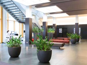 un hall avec de grandes plantes en pot dans un bâtiment dans l'établissement Novotel Karlsruhe City, à Karlsruhe
