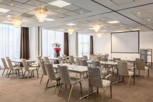 a conference room with tables and chairs and a screen at NH Maastricht in Maastricht