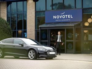 a woman standing next to a car in front of a building at Novotel London Stansted Airport in Stansted Mountfitchet