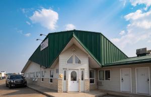 a building with a green roof with a car parked in front at Perfect Inns & Suites in Weyburn