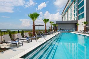 une piscine avec des chaises et des palmiers dans un hôtel dans l'établissement Hyatt Regency Baytown-Houston, à Baytown