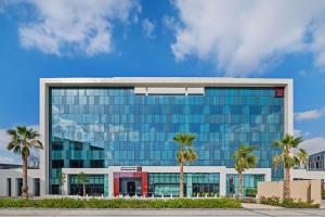 Radisson RED Dubai Silicon Oasis في دبي: مبنى زجاجي كبير أمامه أشجار نخيل
