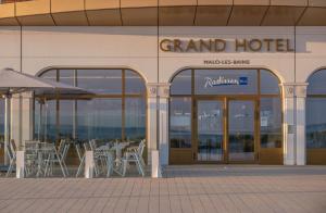 een grand hotel met tafels en stoelen buiten bij Radisson Blu Grand Hotel & Spa, Malo-Les-Bains in Duinkerke