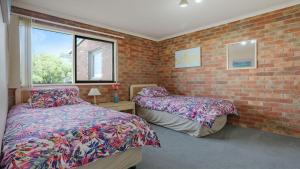 a bedroom with two beds and a brick wall at Unit 6 52 Fishpen Road, Merimbula in Merimbula
