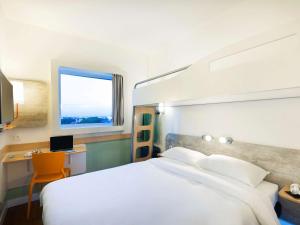 1 dormitorio con cama blanca, escritorio y ventana en ibis budget Campinas Aquidaban, en Campinas