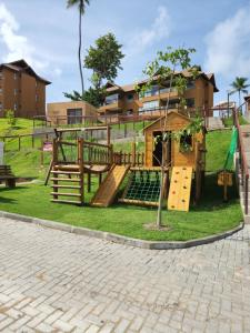 un parque infantil frente a un edificio con un árbol en Eco Resort Praia dos Carneiros - Flat Novo - Ao Lado da Igrejinha, en Praia dos Carneiros