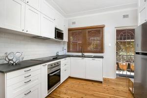 cocina blanca con armarios blancos y suelo de madera en HUNT1 - Great Family Unit, Spacious Green Garden en Sídney