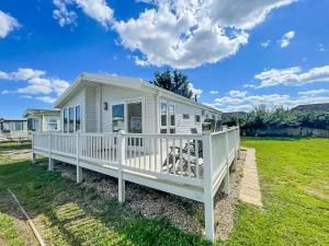a white house with a porch on a lawn at Stunning 4 Berth Lodge With Decking At Breydon Water In Norfolk Ref 10094b in Belton