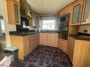 a kitchen with wooden cabinets and a tile floor at Lovely Caravan With Decking At Manor Park, Near Hunstanton Beach Ref 23034c in Hunstanton