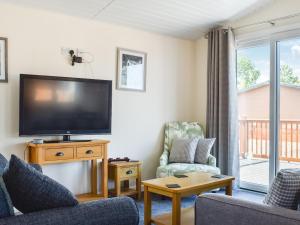 a living room with a flat screen tv and two chairs at Lodge 38 in Stonham Aspall