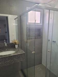 uma casa de banho com um lavatório e uma cabina de duche em vidro. em Apart Guarapari Residence - Areia Preta em Guarapari
