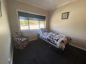 a bedroom with a bed and a chair and a window at 56 Culgoa Crescent, Pambula Beach in Pambula Beach