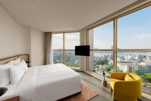1 dormitorio con 1 cama blanca y 1 silla amarilla en L7 WEST LAKE HANOI By LOTTE en Hanói