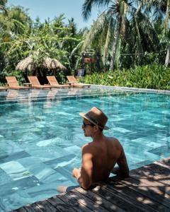 un hombre con sombrero sentado junto a una piscina en Hoi An Eco Lodge & Spa en Hoi An