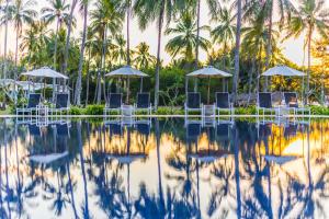 einen Pool mit Stühlen, Sonnenschirmen und Palmen in der Unterkunft Kantary Beach Hotel Villas & Suites in Khao Lak