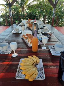 una mesa de madera con platos de plátanos y zumo de naranja en Pension LE PASSAGE vue jardin, en Vaitoare