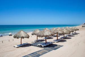 a row of straw umbrellas and chairs on a beach at Luxury Oceanview Condo - Las Palomas - Pool, Golf, Sandy Beach ! in Puerto Peñasco