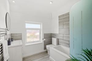 a bathroom with a tub and a toilet and a window at Spacious 2 bedroom house with parking & WiFi in Kent