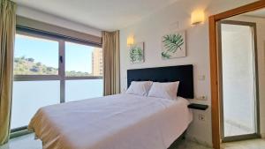 ein Schlafzimmer mit einem weißen Bett und einem großen Fenster in der Unterkunft Moderno apartamento con terraza privada y vistas in Benidorm