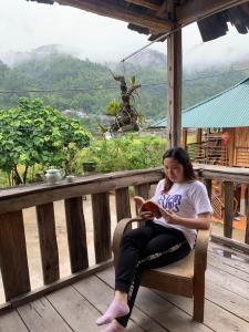 A Lử Homestay في Mù Cang Chải: امرأة تجلس على الشرفة تقرأ الكتاب
