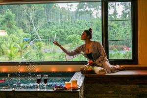 Una donna seduta davanti a una finestra di fronte a una piscina di Niyatma Wayanad Premium Coffee Resort By VOYE HOMES a Wayanad