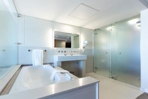uma casa de banho branca com um lavatório e um chuveiro em Blaauwberg Beach Hotel em Bloubergstrand