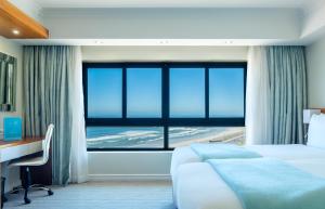 a hotel room with a bed and a desk and a large window at Blaauwberg Beach Hotel in Bloubergstrand