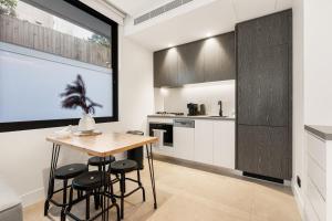 uma cozinha com armários brancos, uma mesa de madeira e bancos em THE SHORE (1): COOGEE BEACH em Sydney