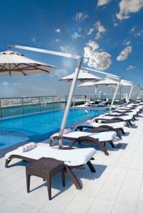 eine Reihe von Liegestühlen und Sonnenschirmen neben einem Pool in der Unterkunft Park Regis Kris Kin Hotel in Dubai