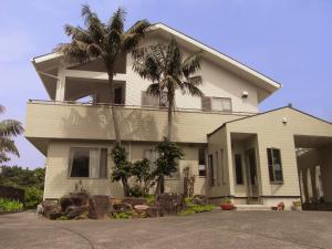 a white house with palm trees in front of it at Kencha Rumah in Hachijo