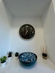 Elbląska Noclegi في لودز: ساعة سوداء على جدار أبيض فيه نباتات