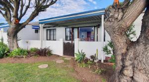 a white house with a tree in front of it at Paradise Beach Cottage in Jeffreys Bay