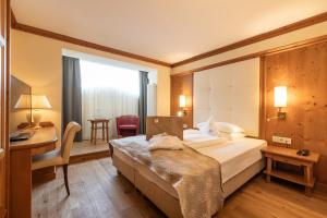 オルティゼーイにあるアルピン ＆ ヴィタル ホテル ラ ペルラのベッドとデスクが備わるホテルルームです。