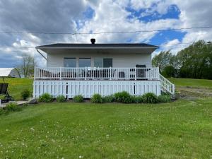 une maison blanche avec une terrasse couverte et une cour dans l'établissement Chalets Plage St-Jean 2, à Saint-Jean