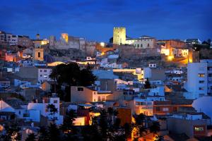 una ciudad iluminada por la noche con un castillo en LA TRAVIATA - Buñol, en Buñol