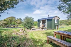 a green barn with a picnic table and benches at Haven View - 1 Bedroom Shepherds Hut - St Ishmaels in Saint Ishmaels
