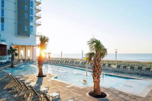 a swimming pool with palm trees next to the beach at Hilton Grand Vacations Club Ocean Enclave Myrtle Beach in Myrtle Beach