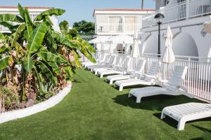 a row of white lounge chairs on the lawn at a hotel at Bungalows Parque Nogal in Maspalomas