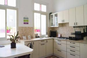 eine Küche mit weißen Schränken, einem Tisch und Fenstern in der Unterkunft Ajami Guest House in Tel Aviv