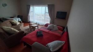 a bedroom with a red bed and a living room at Huisie Langs Die See in Swakopmund