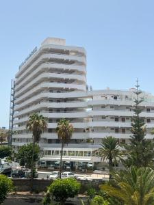 a large white building with palm trees in front of it at The White Waves TF Holiday Apartment Las Americas in Playa Fañabe