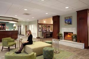 Hampton Inn & Suites Providence-Warwick Airport في وارويك: امرأة تجلس على أريكة في غرفة انتظار